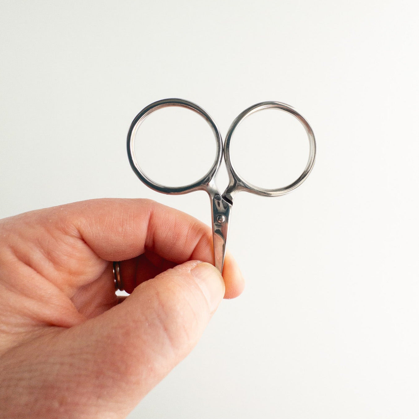 Hand holding a small pair of scissors against a white background