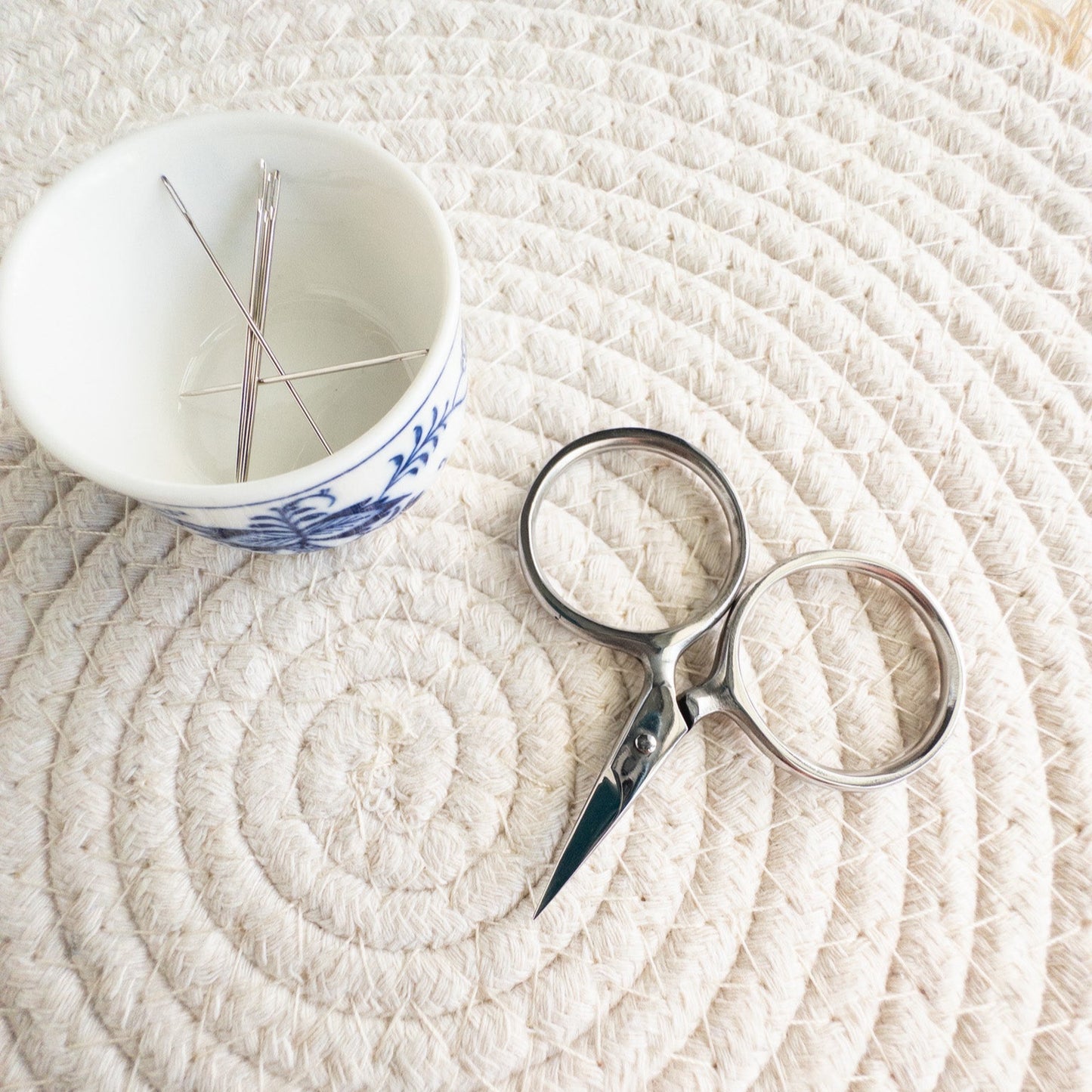 Scissors and a small cup with needles on a textured white surface