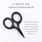 Black scissors with a primitive-style design on a white background, accompanied by text that says "These scissors feature a primitive-style design with a stamped pattern intentionally reflecting a worn, aged look in certain areas."