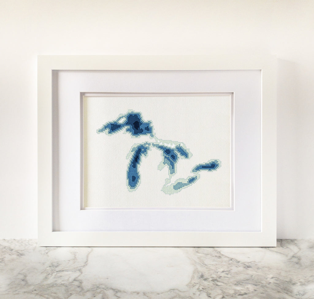 Framed Great Lakes cross-stitch art with blue bathymetric lake map on white fabric.