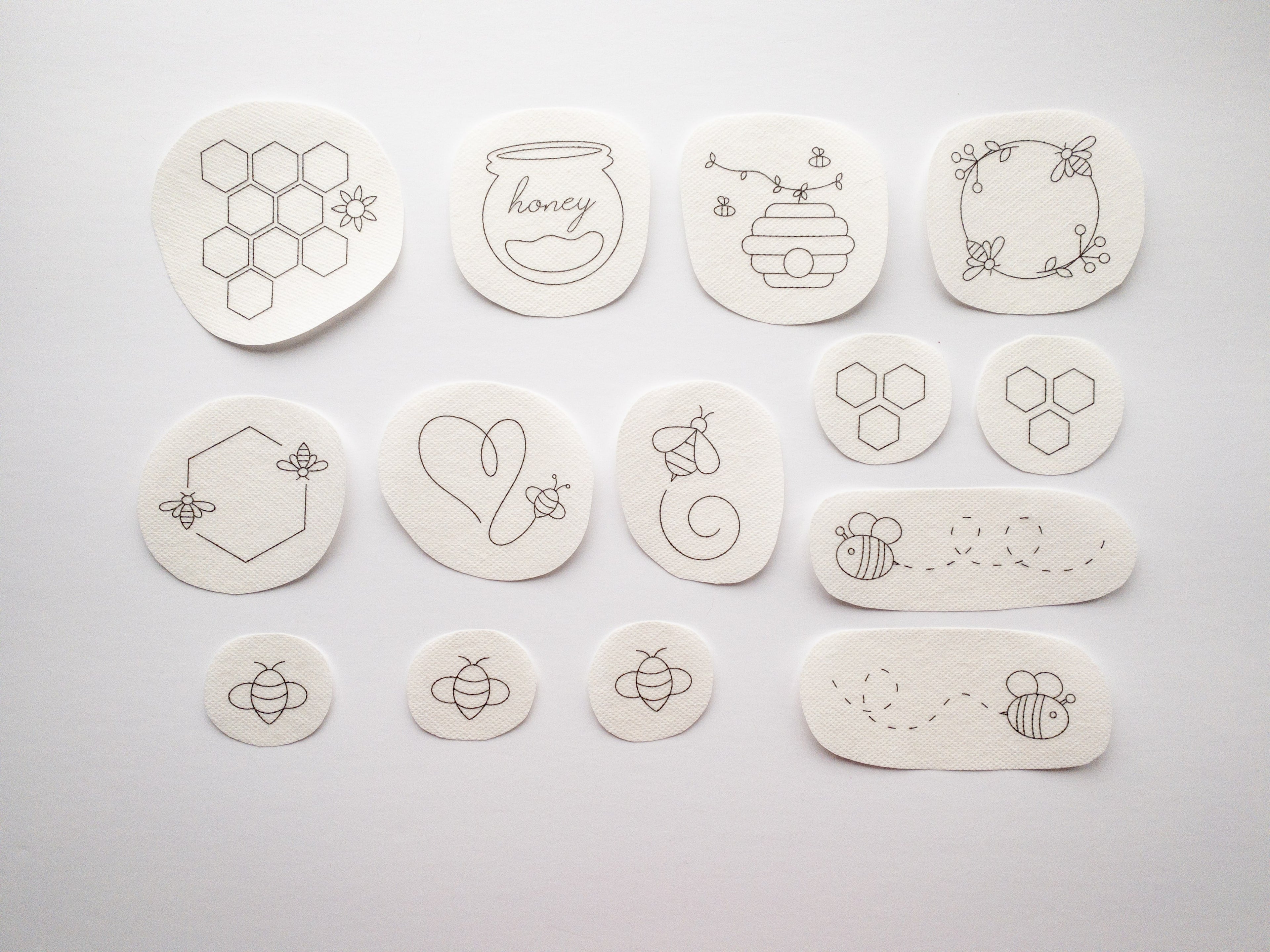 14 white water-soluble stick and stitch patches with black honeybee-themed embroidery designs.