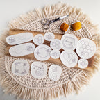 14 white water-soluble stick and stitch bee embroidery patterns on a wooden board with thread and scissors.