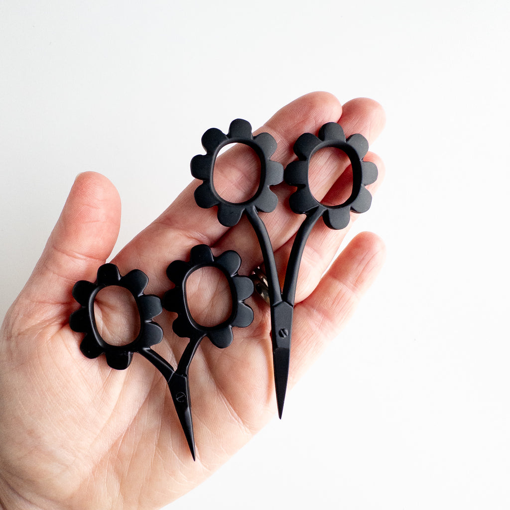 Black floral-handled scissors held in a hand against a white background