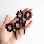 Black floral-handled scissors held in a hand against a white background