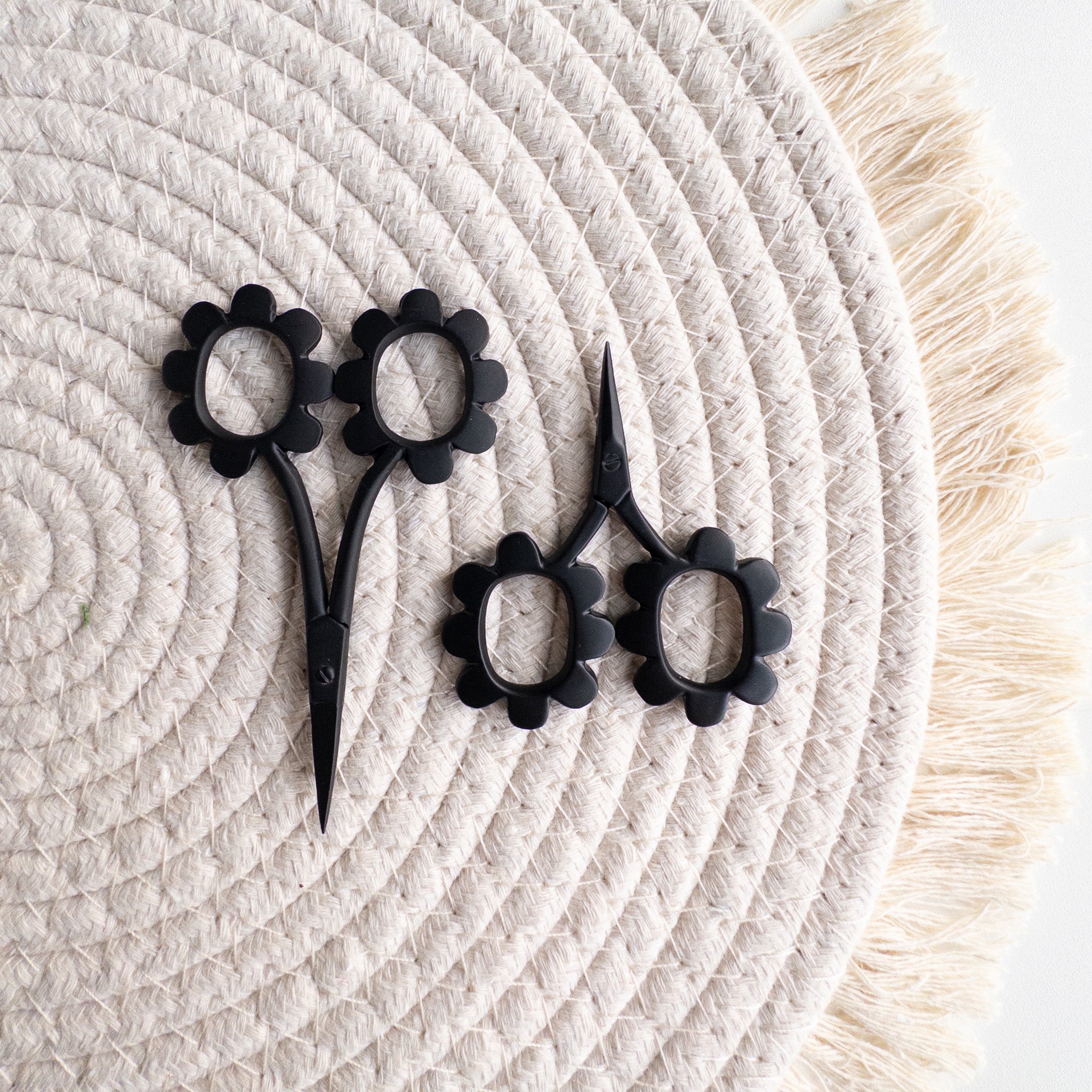 Two different sized black floral scissors on a woven cream-colored mat