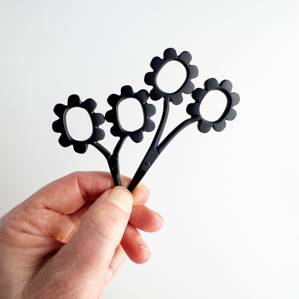 Black flower-shaped tool held by a hand against a white background