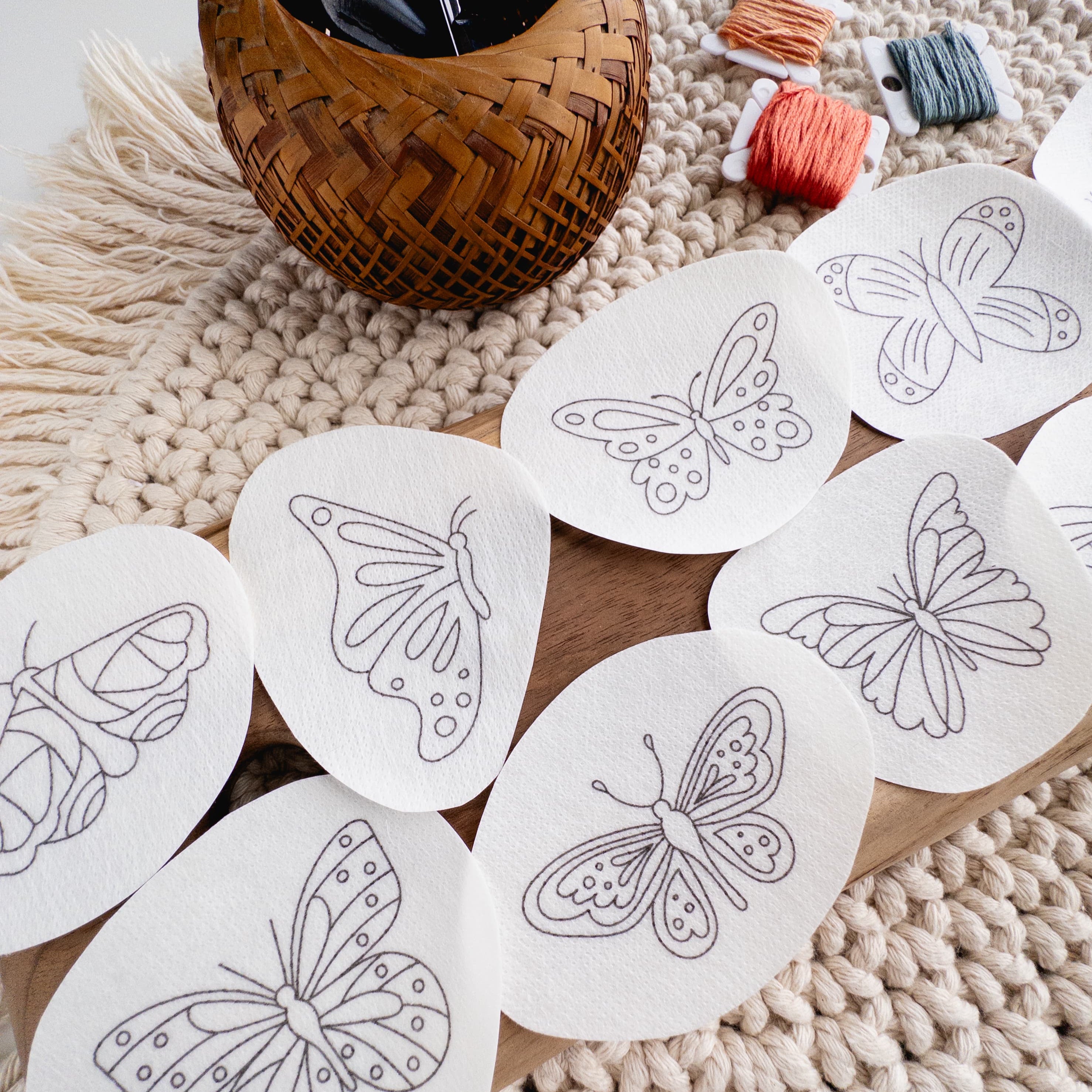 White water-soluble stick and stitch butterfly embroidery patterns on a wooden board with yarn and a basket.