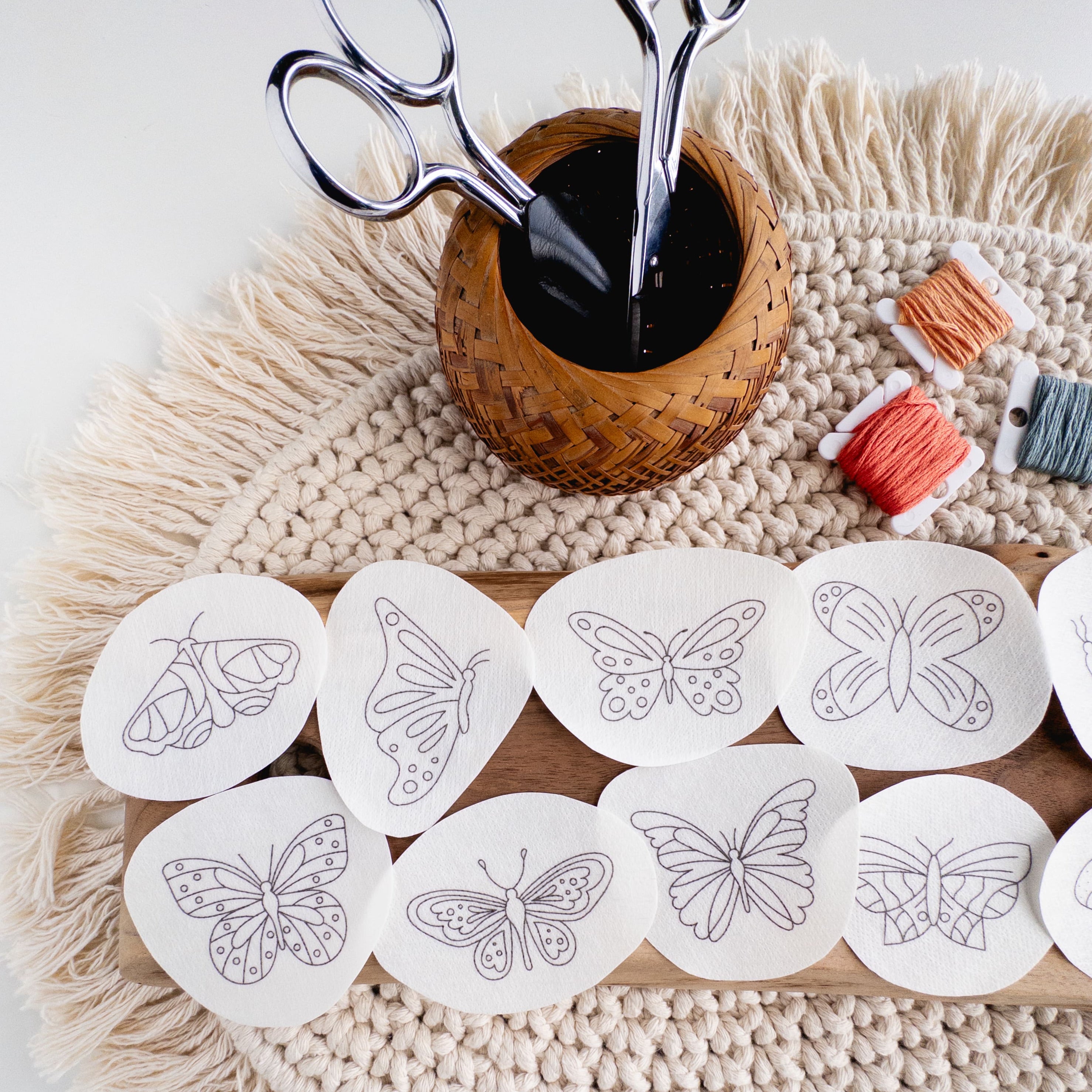 Twelve white water-soluble butterfly embroidery patterns on a wood board, with scissors and floss.
