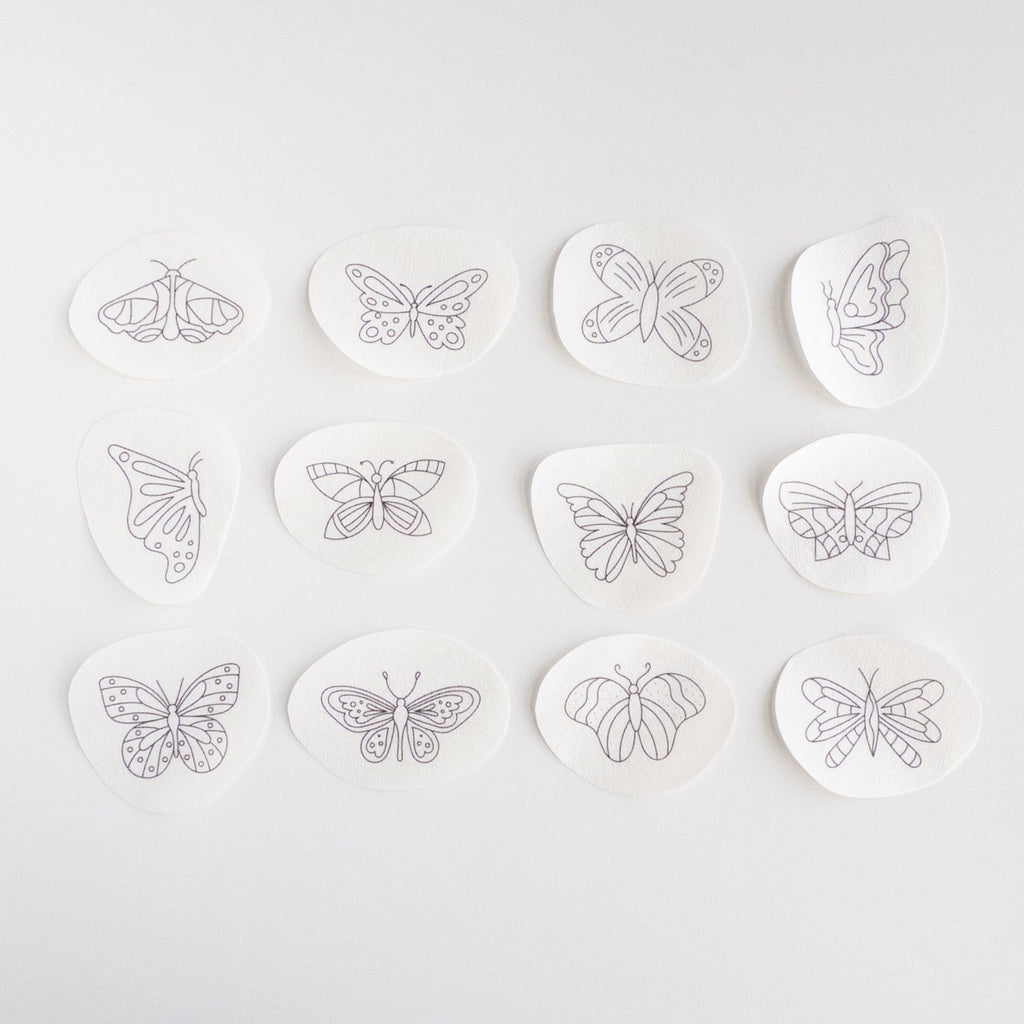 Twelve white water-soluble stick and stitch butterfly embroidery patterns with black outlines, ranging from 1.3" to 2.3" wide.