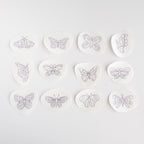 Twelve white water-soluble stick and stitch butterfly embroidery patterns with black outlines, ranging from 1.3" to 2.3" wide.