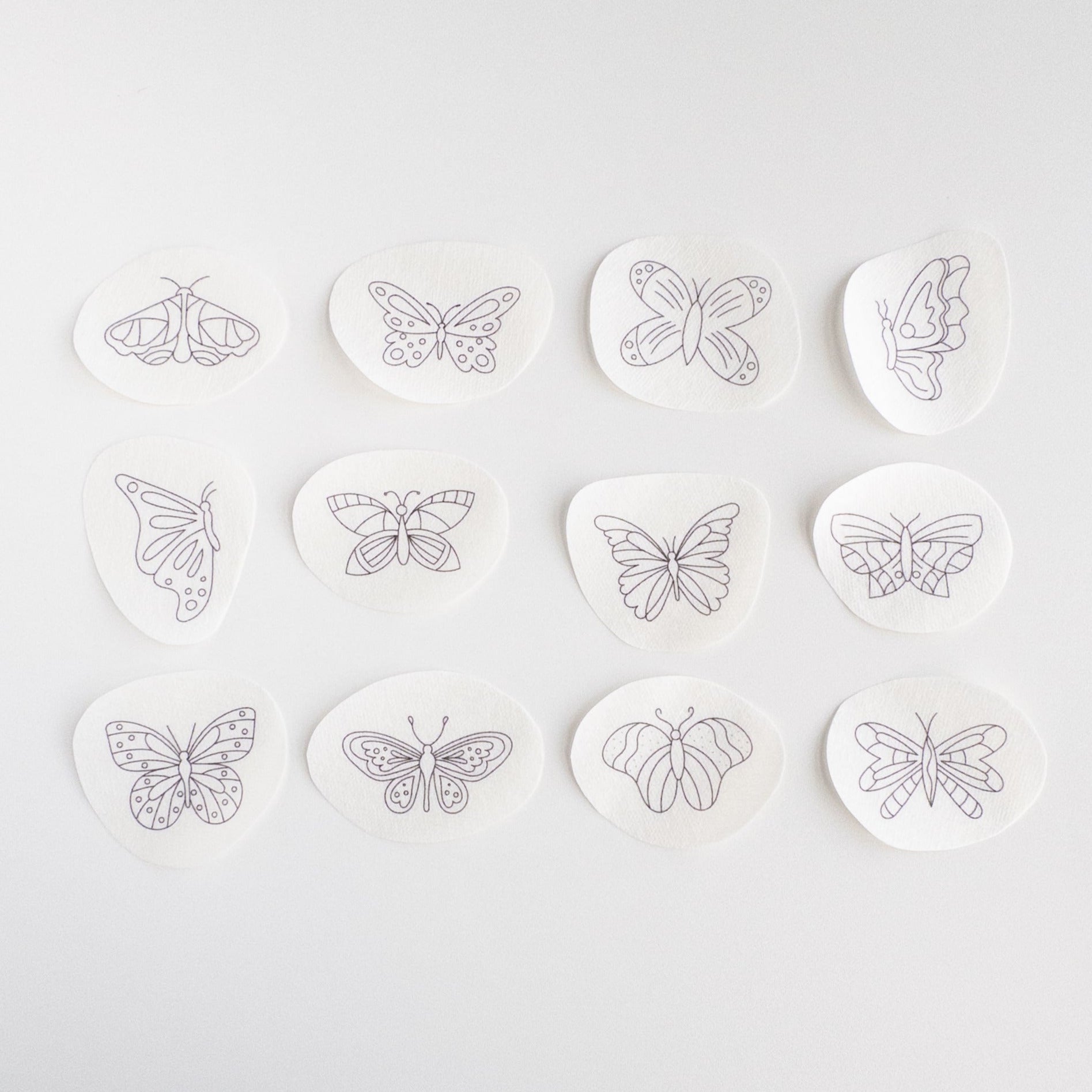 Twelve white water-soluble stick and stitch butterfly embroidery patterns with black outlines, ranging from 1.3" to 2.3" wide.