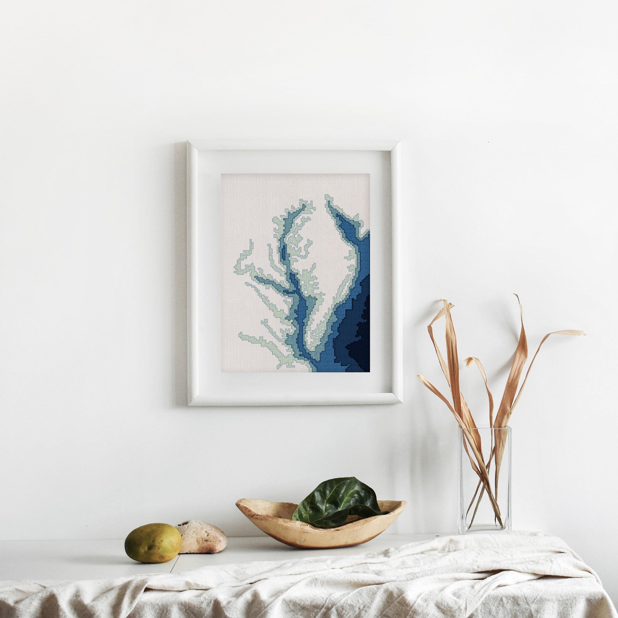 Framed Chesapeake Bay cross-stitch pattern, a minimalist blue bathymetry map on white fabric.