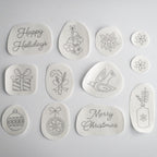 12 white water-soluble stick and stitch Christmas embroidery patterns, including "Happy Holidays," bells, poinsettias, a gift, candy cane, dove, ornaments, "Merry Christmas," and a vase.