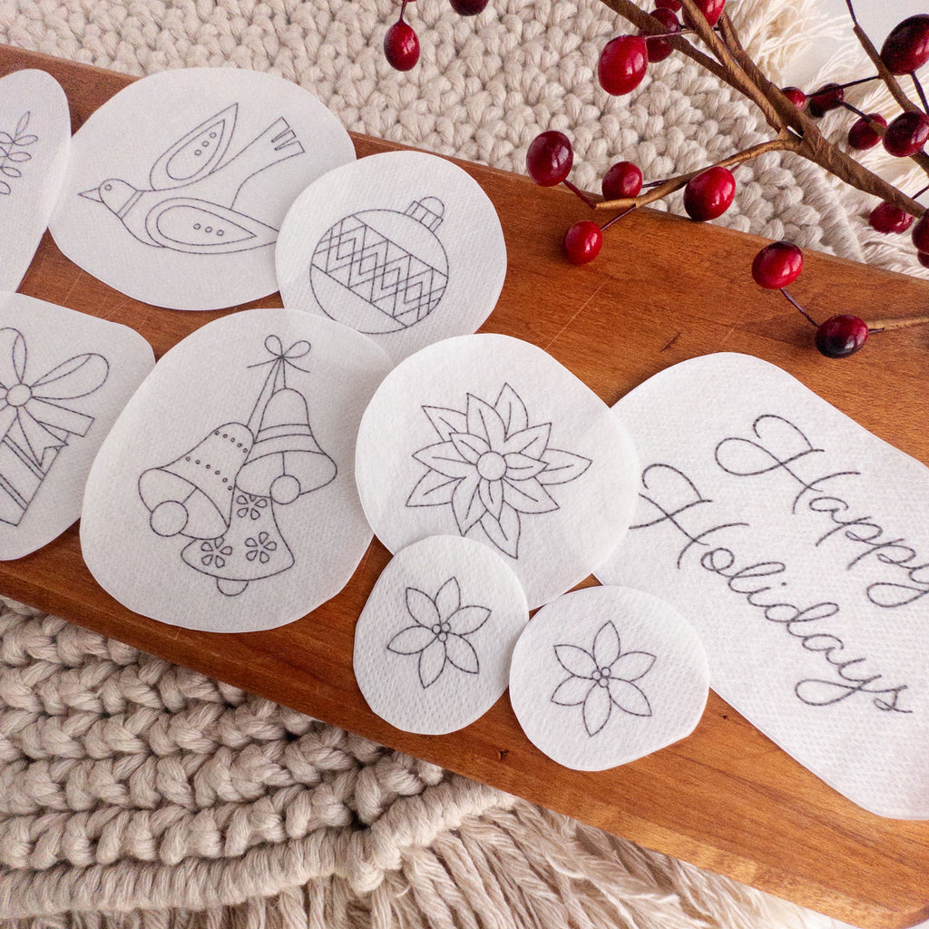 White water-soluble stick and stitch Christmas embroidery patterns on a wooden board with red berries.