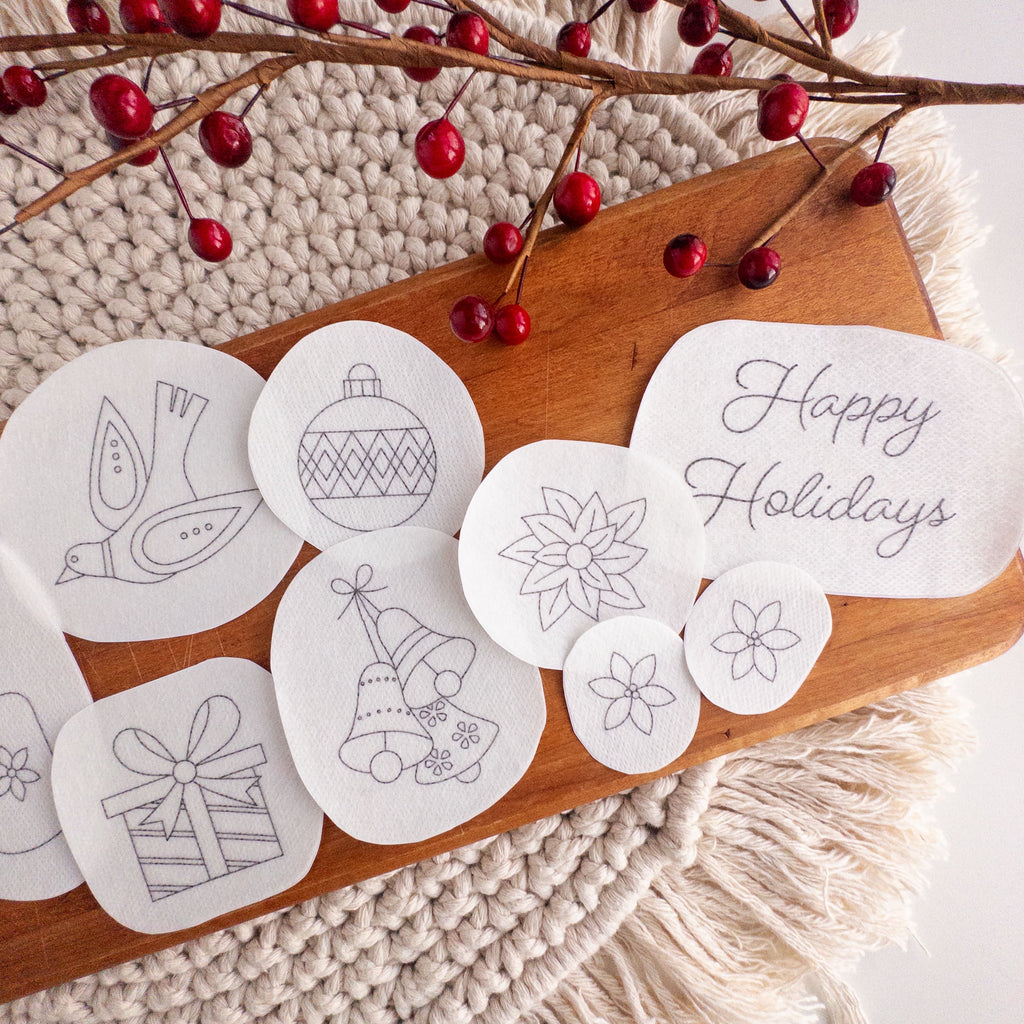 White water-soluble Christmas stick and stitch embroidery patterns on a wooden board with red berries.
