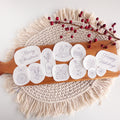 12 white water-soluble Christmas stick and stitch embroidery patterns on a wooden board with red berries.