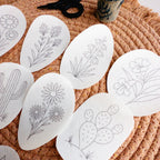 White desert botanical embroidery stick and stitch patterns on a woven mat, featuring cacti, succulents, and blooms.