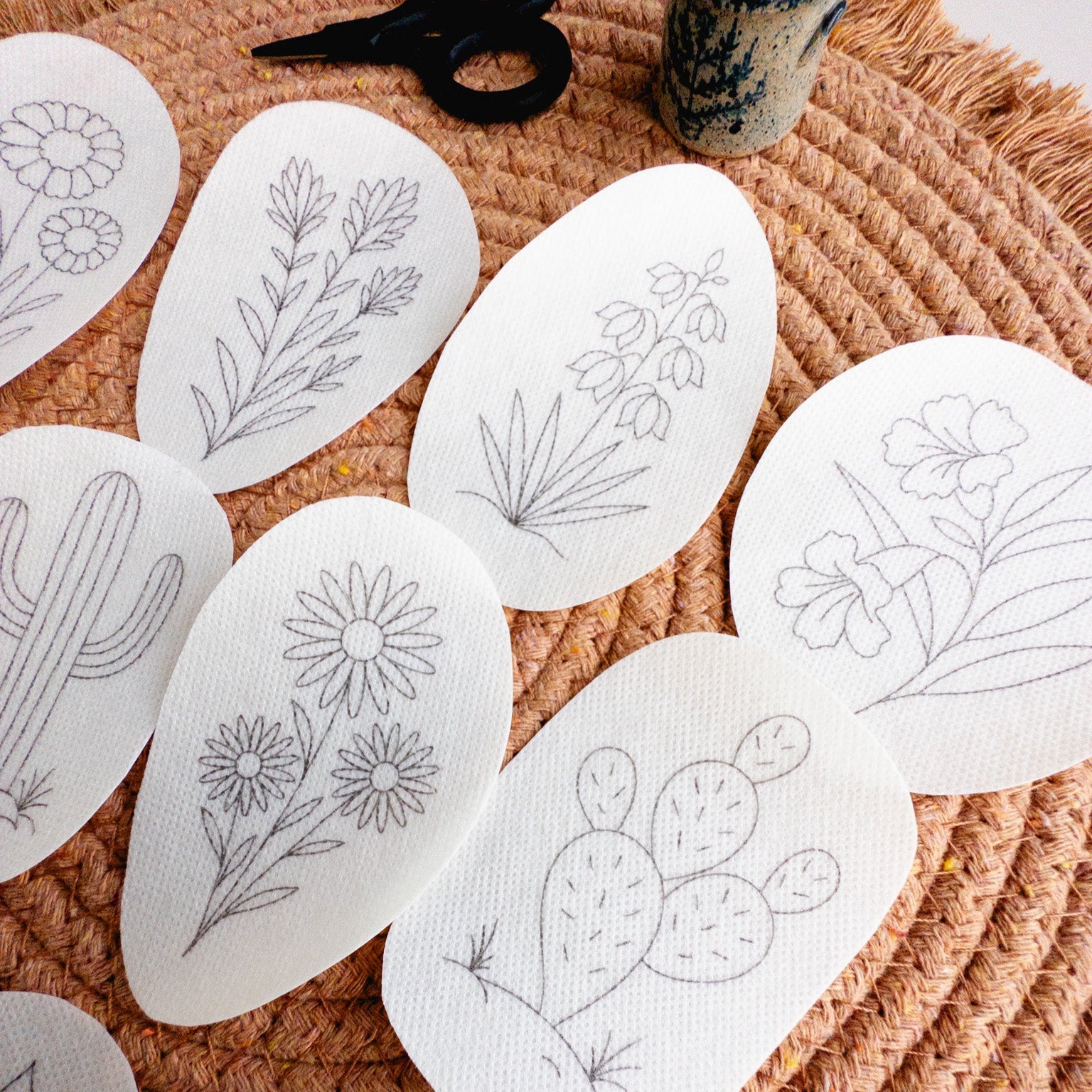 White desert botanical embroidery stick and stitch patterns on a woven mat, featuring cacti, succulents, and blooms.