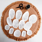White desert botanical embroidery stick and stitch patterns, including cacti and flowers, on a fringed brown placemat with scissors and needles.