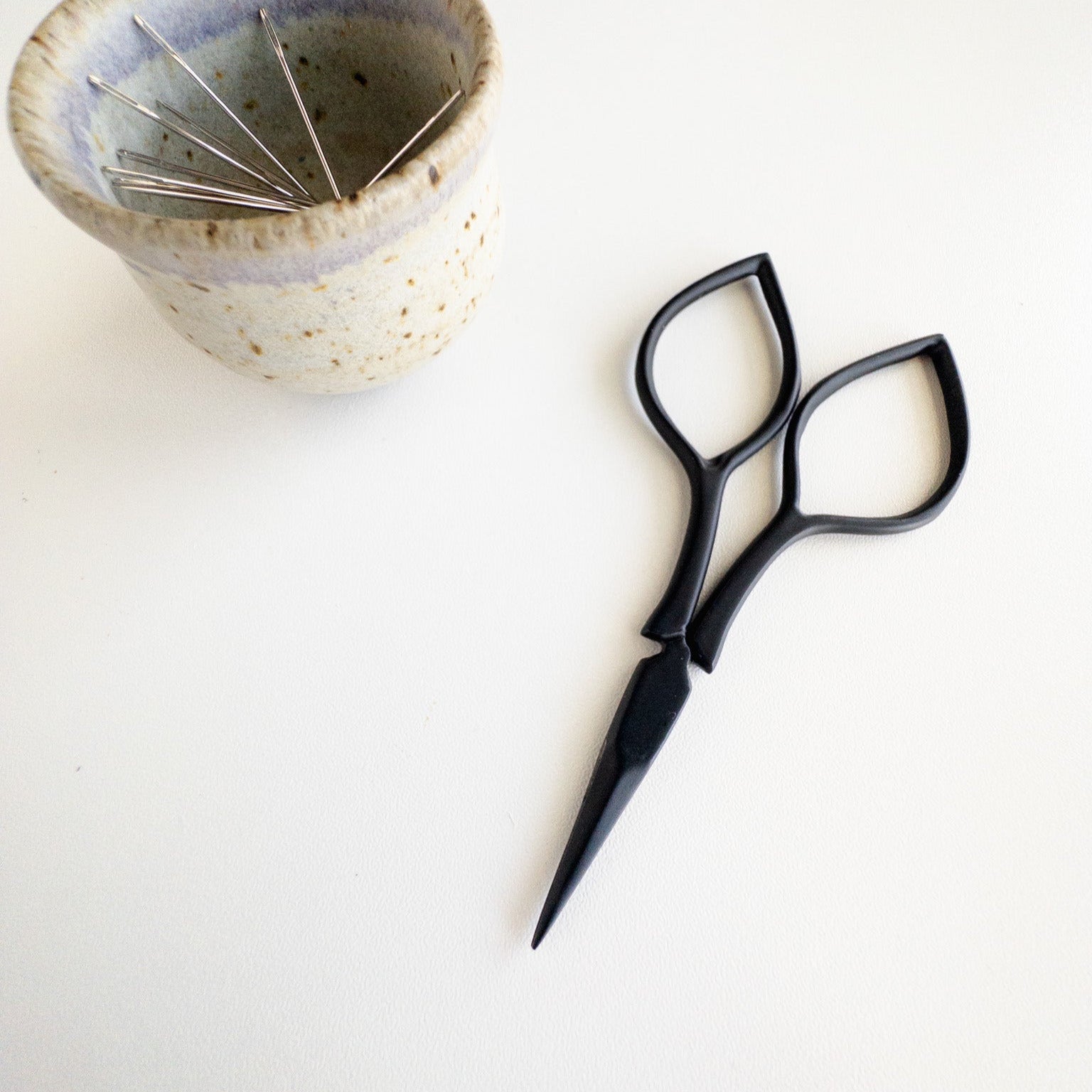 Black scissors and a ceramic bowl on a white background