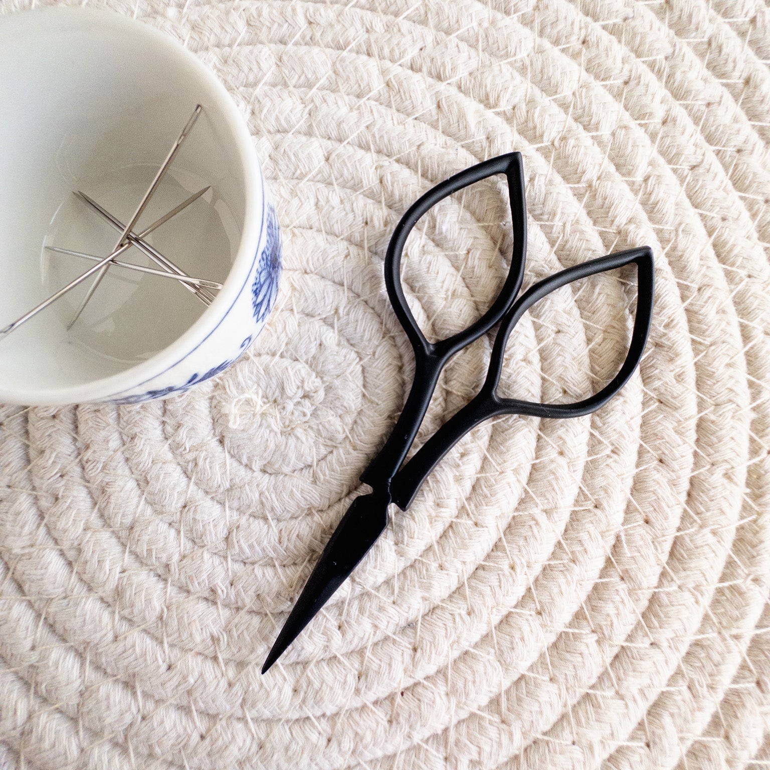 Black scissors on a textured white surface with a white cup in the background