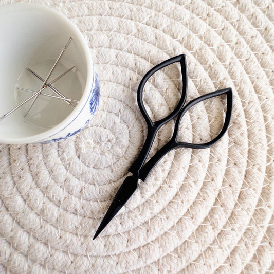 Black scissors on a textured white surface with a white cup in the background
