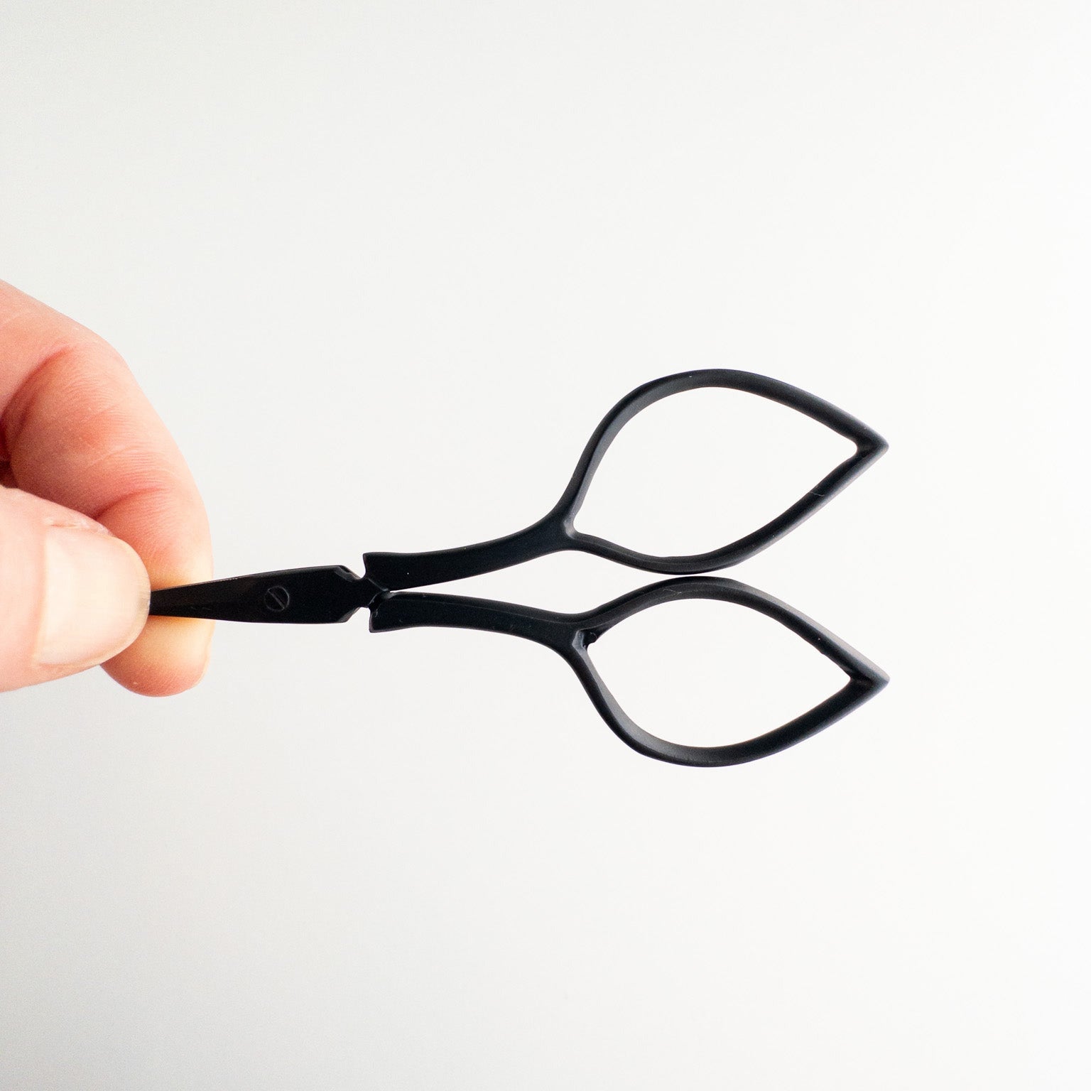 Matte black embroidery scissors held by a person.