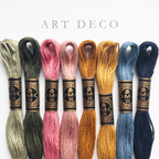 Eight spools of DMC Art Deco embroidery floss in green, pink, gold, and blue shades.