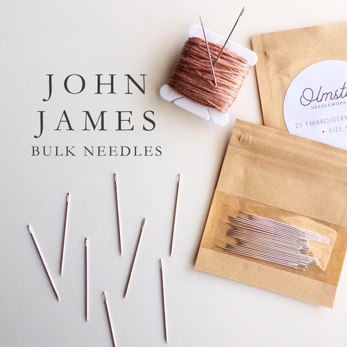 Silver John James embroidery and chenille needles, some loose, some in a clear-front bulk pack.