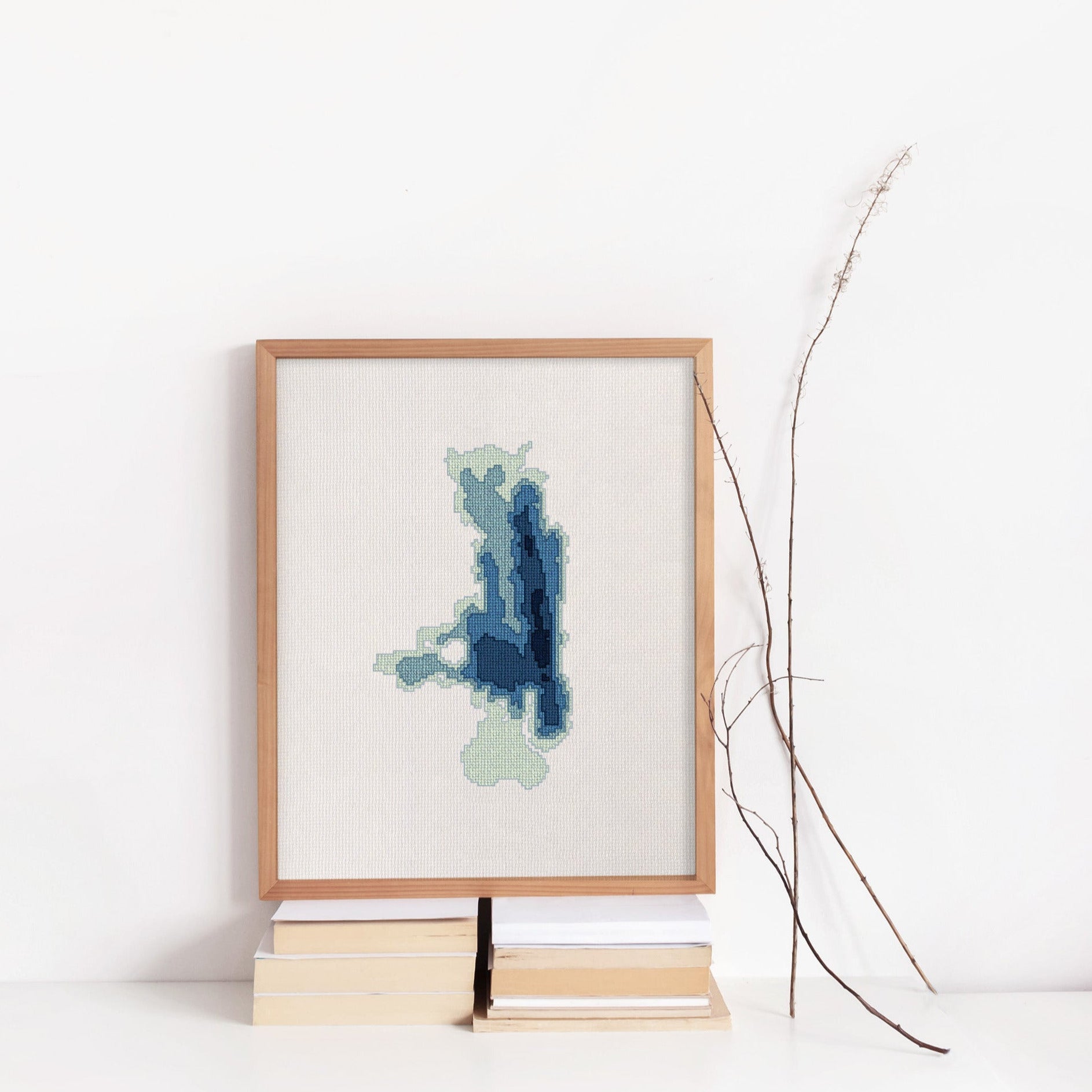 Framed Flathead Lake cross-stitch pattern in shades of blue and green, displayed on books.
