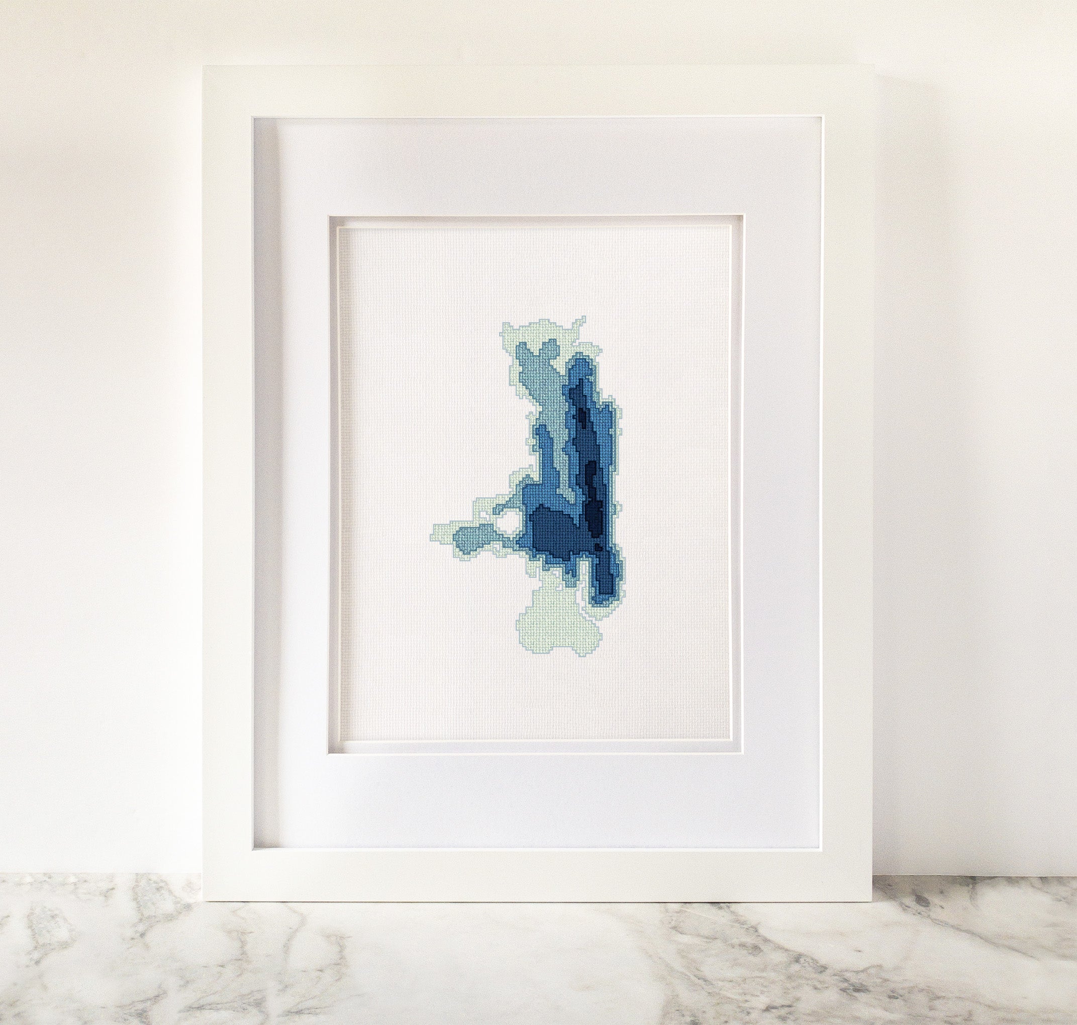 Framed Flathead Lake cross-stitch art with minimalist blue and green bathymetric map design.