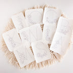 White stick and stitch embroidery patterns featuring large floral letters K, M, N, S, O, C, L, B, A on a macrame mat.