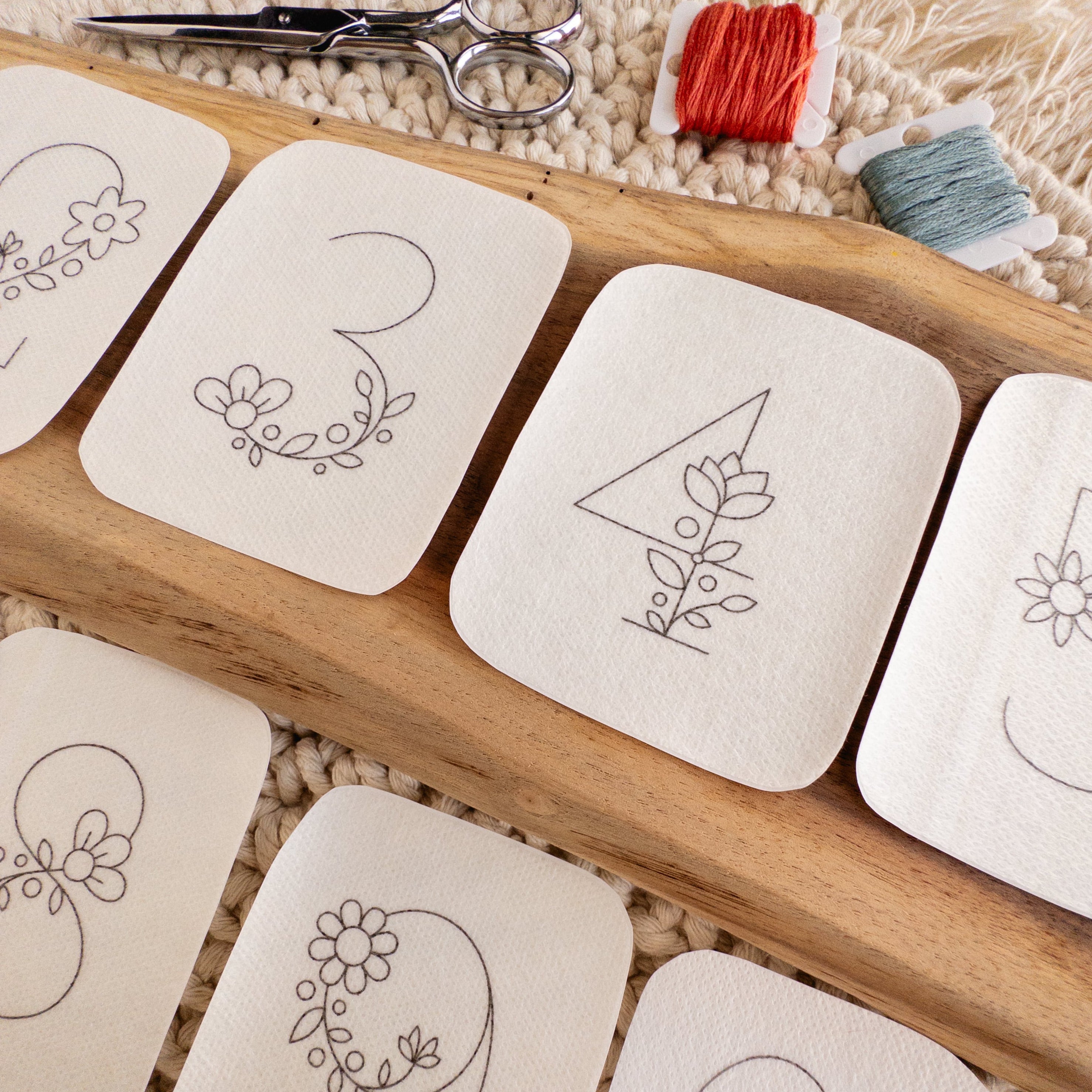 White stick and stitch embroidery patterns featuring floral numbers 0-9, with scissors and floss.