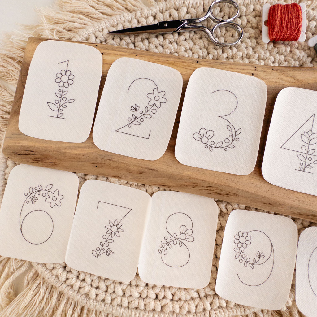 Floral numbers 1-9 stick and stitch embroidery patterns on a wooden board with scissors and thread.