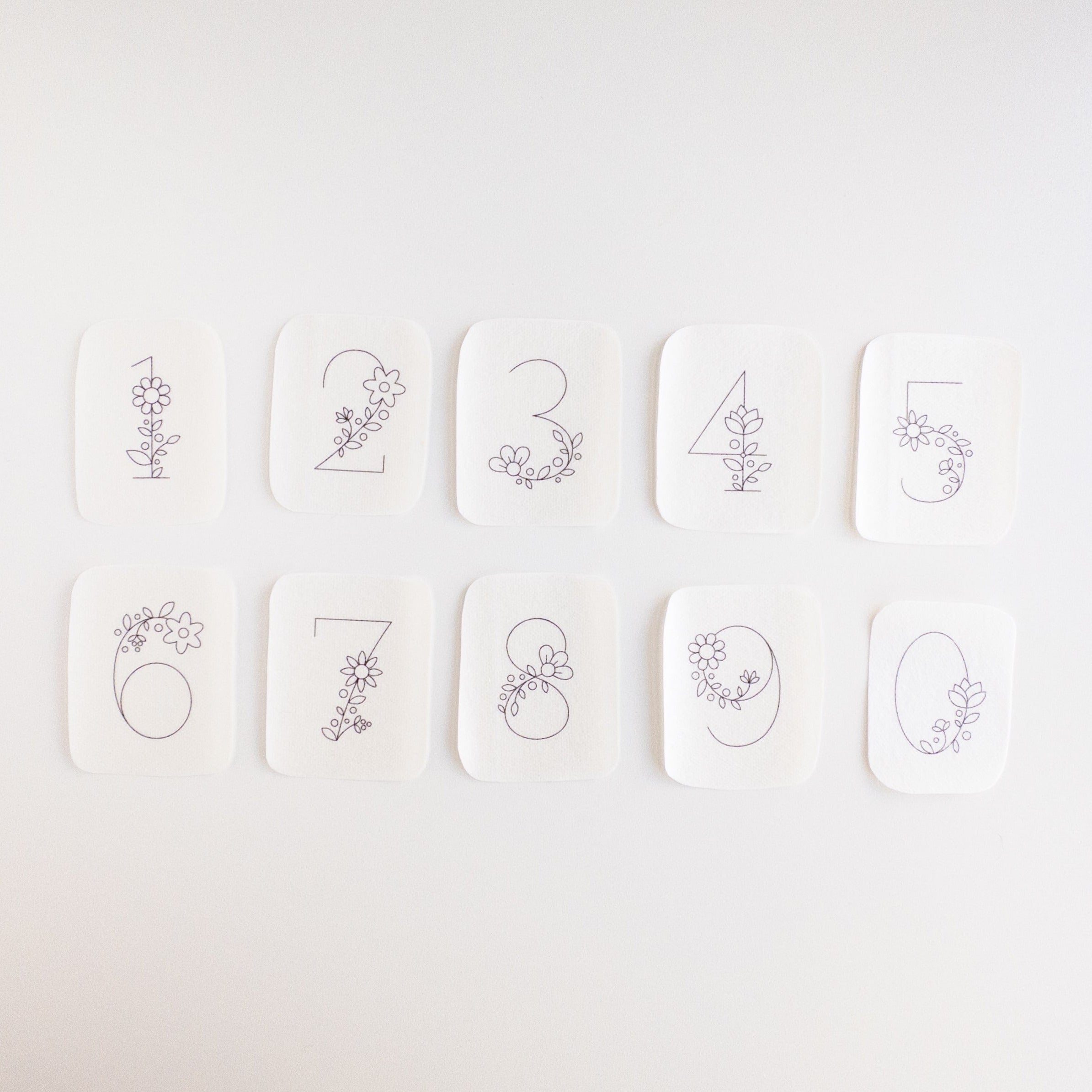 Ten white stick and stitch embroidery patterns, each with a floral-decorated number from 0 to 9.