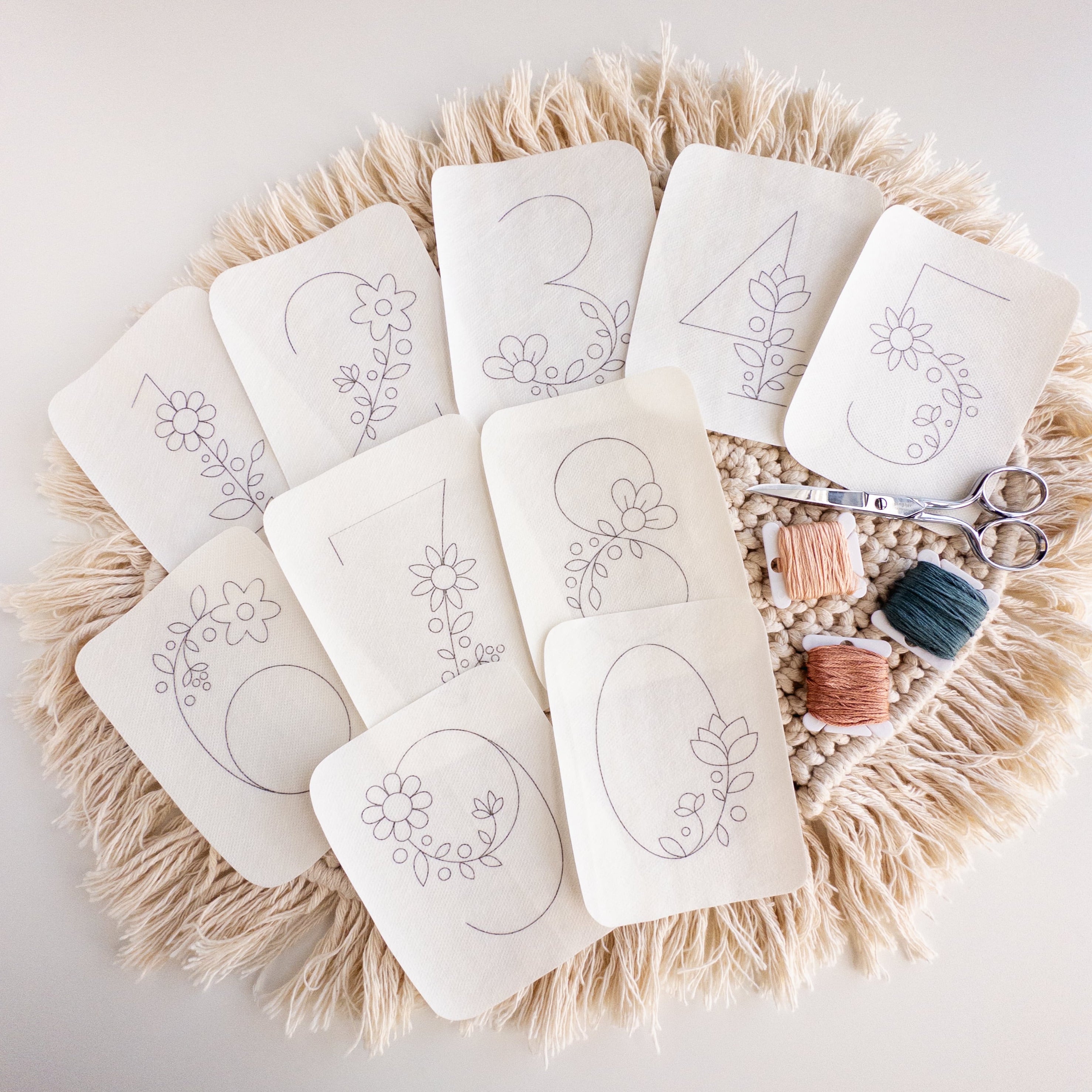 Floral number stick and stitch embroidery patterns 0-9, with floss and scissors on a macrame mat.