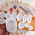 Hand holding a white folk flower embroidery sticker with other floral patterns, thread, and scissors on a wooden board.
