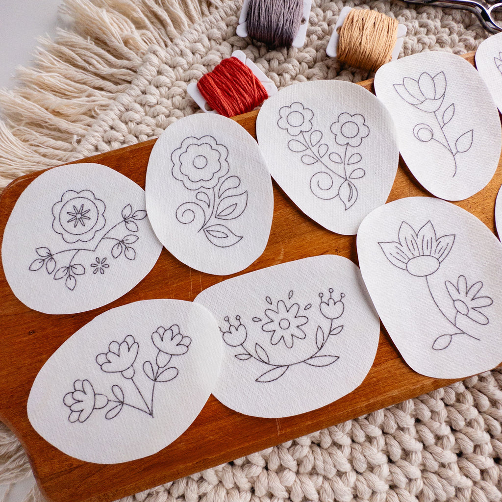 Scandinavian folk flower embroidery patterns on water-soluble stabilizer stickers, with floss and scissors.