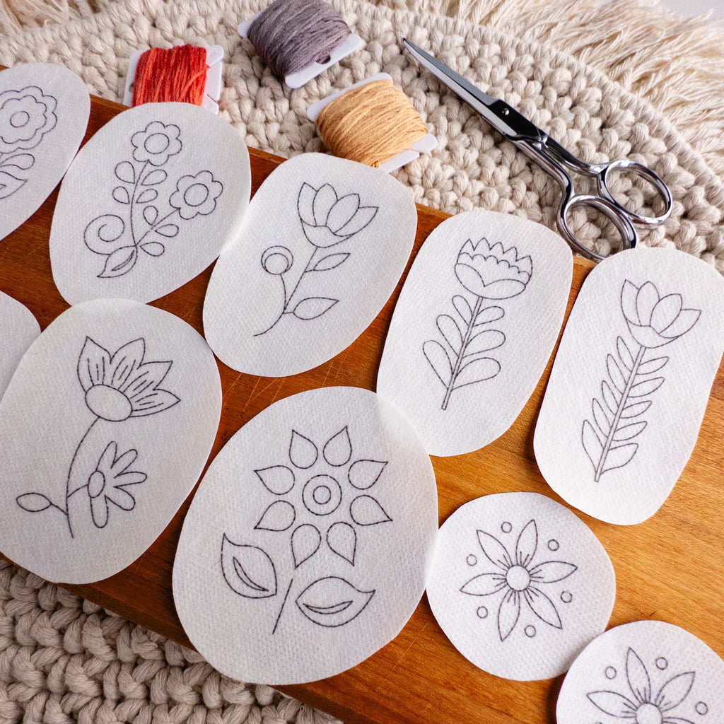 Scandinavian folk flower stick and stitch embroidery patterns on a wooden board with floss and scissors.