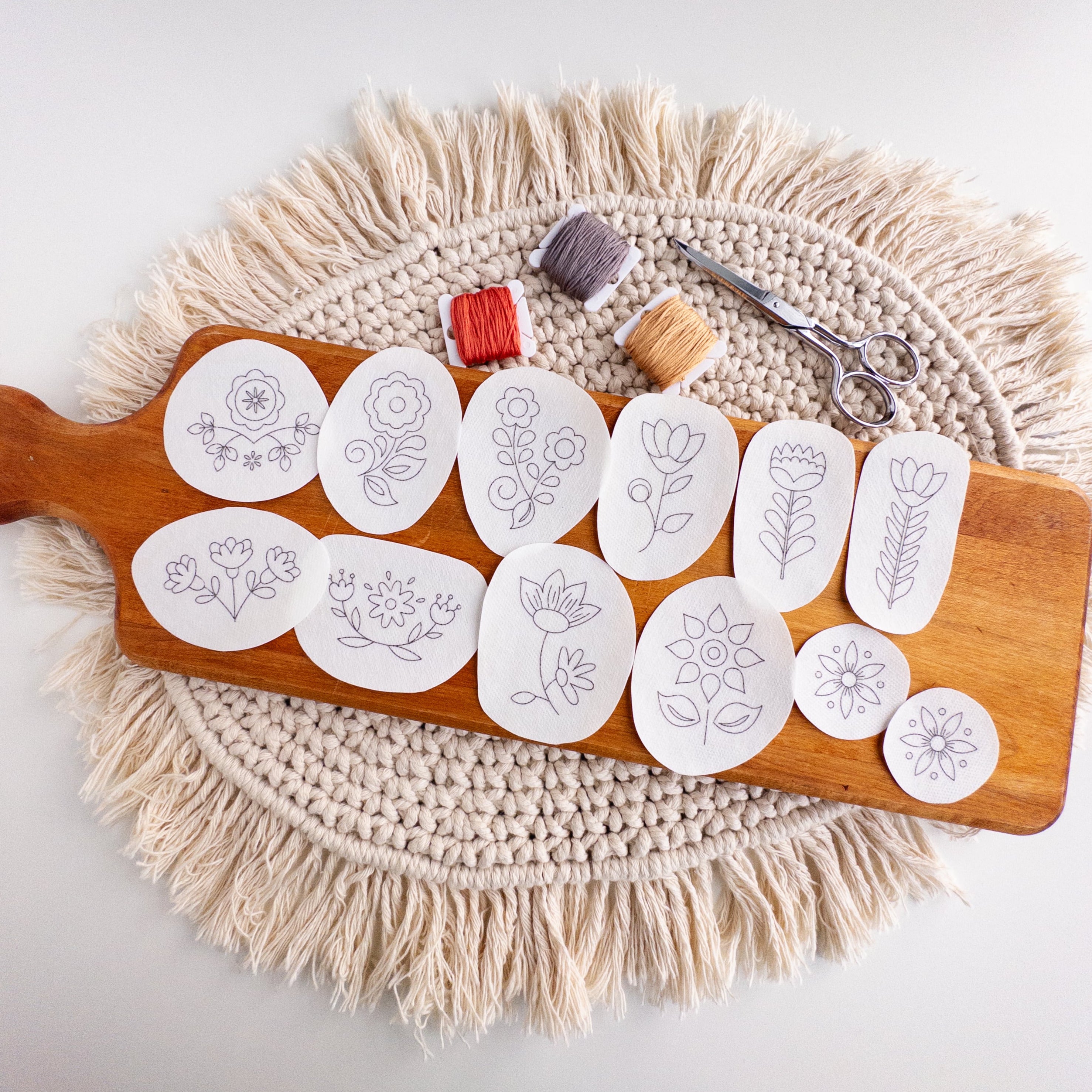 12 Scandinavian folk flower embroidery patterns on white water-soluble stabilizer stickers, with floss and scissors.