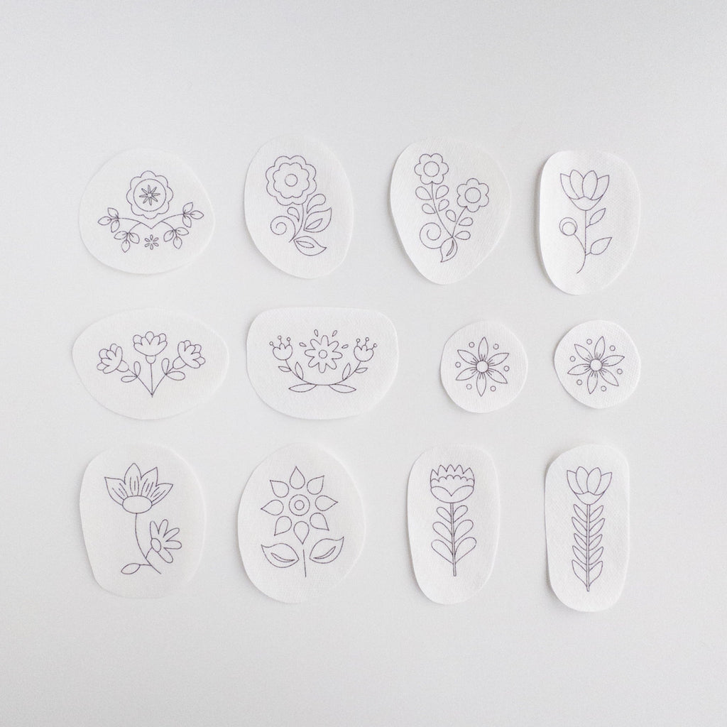 12 white water-soluble stabilizer stickers with purple Scandinavian folk flower embroidery patterns.