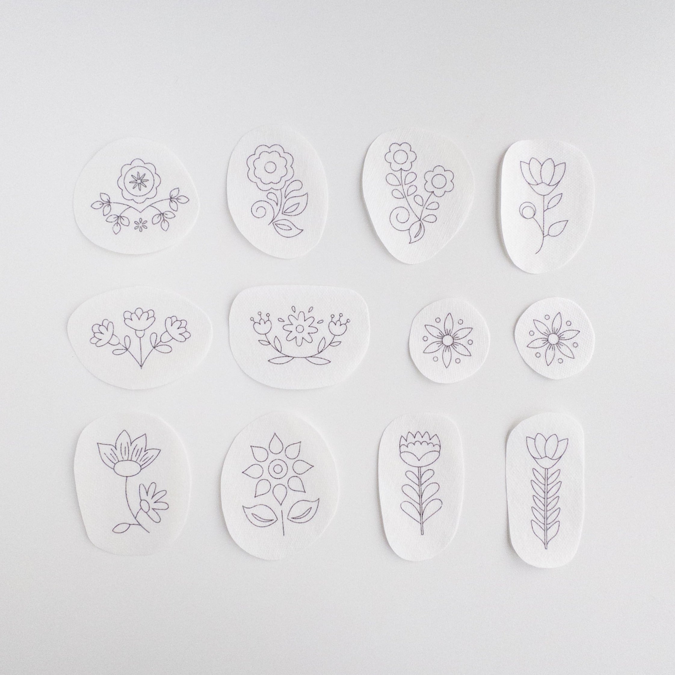 12 white water-soluble stabilizer stickers with purple Scandinavian folk flower embroidery patterns.