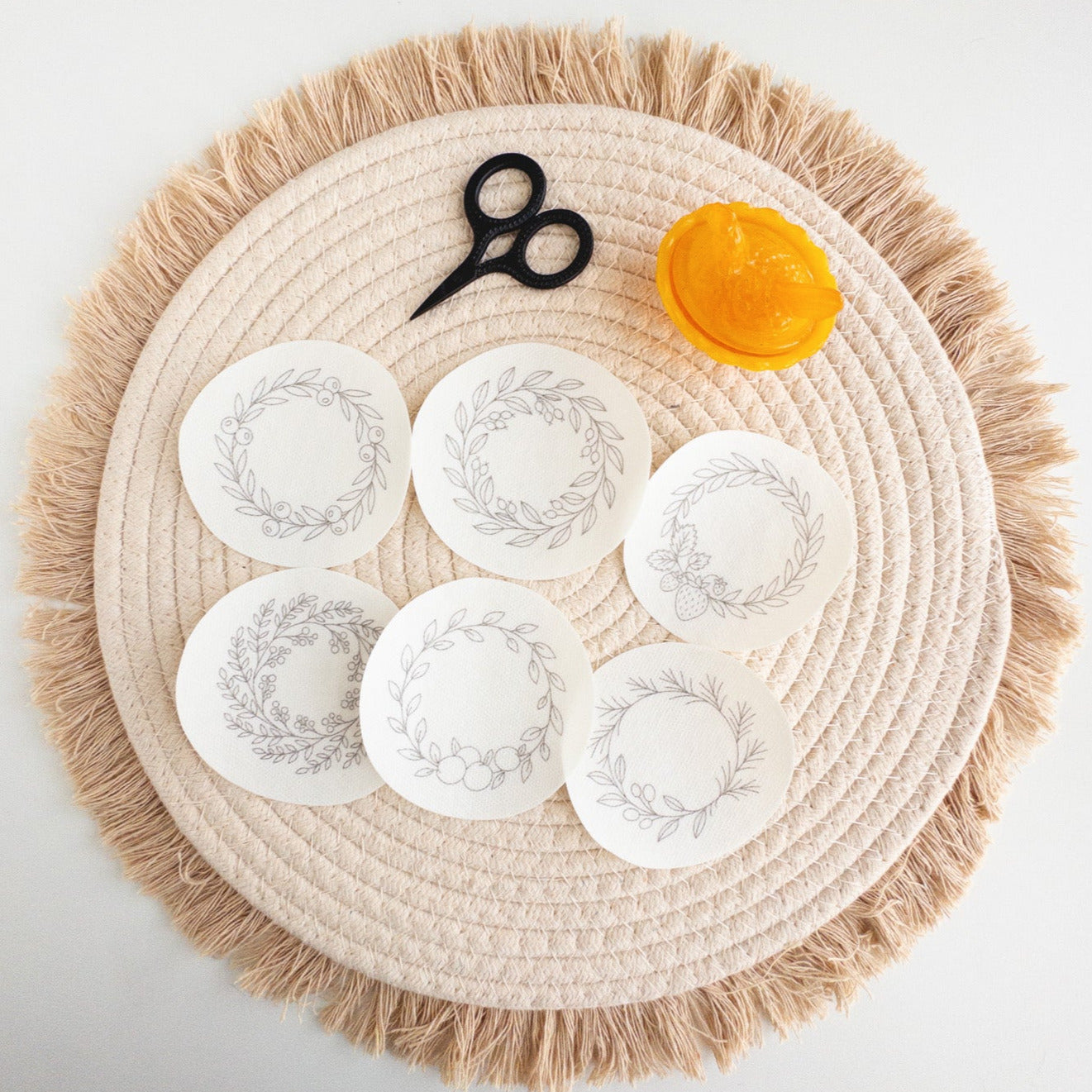 Six round, white wash-away embroidery stickers with delicate fruit wreath designs on a woven placemat.