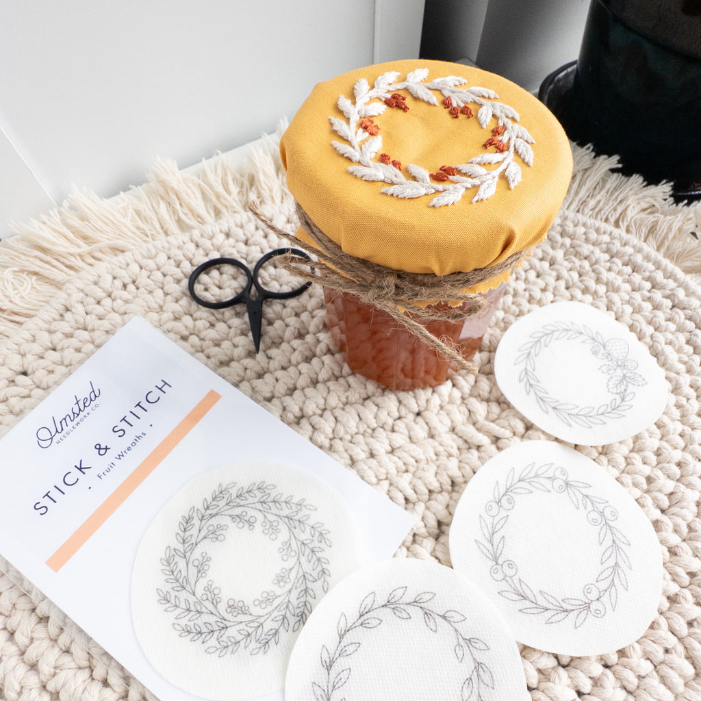 Embroidered fruit wreath jam jar topper with wash-away patterns, scissors, and a crochet mat.