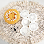 Embroidered fruit wreath on yellow fabric, with five wash-away patterns and small black scissors on a macrame mat.