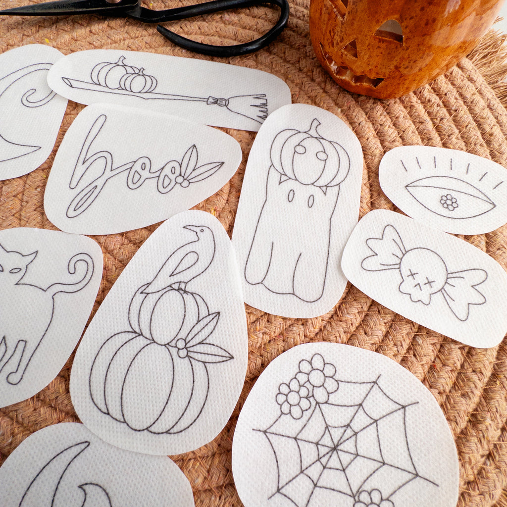 White water-soluble embroidery patches with 12 black Halloween designs like pumpkins, ghosts, and "boo.