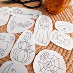 White water-soluble embroidery patches with 12 black Halloween designs like pumpkins, ghosts, and "boo.