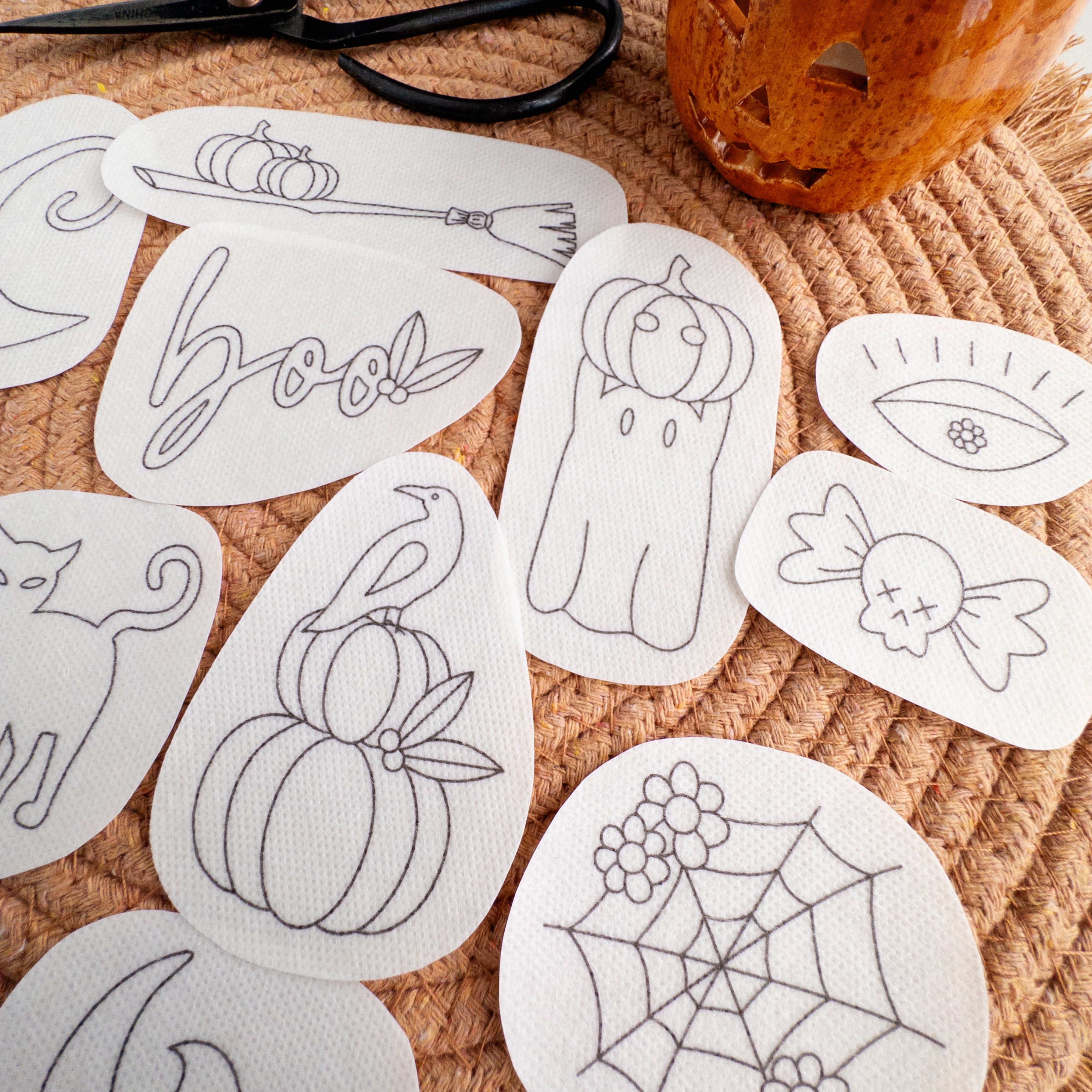 White water-soluble embroidery patches with 12 black Halloween designs like pumpkins, ghosts, and "boo.