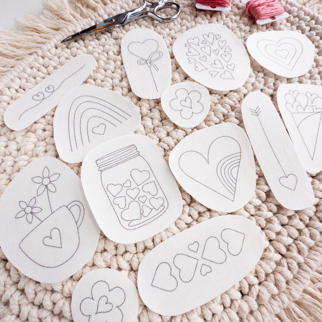 13 white water-soluble heart embroidery stick and stitch patterns, various designs, on a cream textured mat.