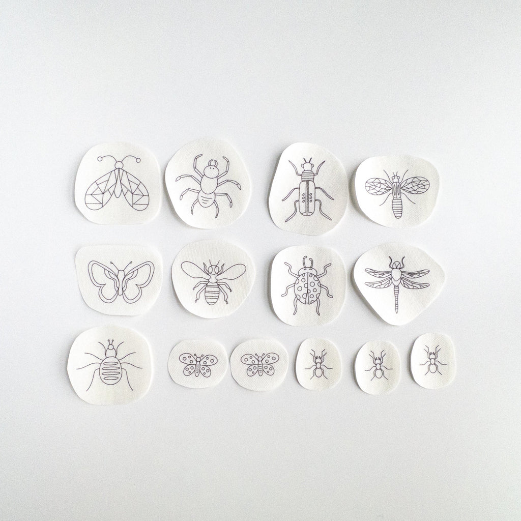 14 black outline insect embroidery patterns on white water-soluble stabilizer patches, assorted bug designs and sizes.